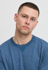 Blauwe gebreide sweater met een ronde halslijn en geribbelde manchetten. Heeft een gestructureerde stof en een contrasterend tonale detail op de schouder.