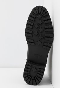 Semelle noire robuste d'une botte avec des rainures profondes et des motifs en forme de croix, taille 37, nom de marque "Anna Field" visible.