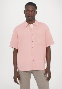 Short-sleeve, button-up shirt in light pink fabric with a textured finish, featuring a chest pocket and wooden buttons.