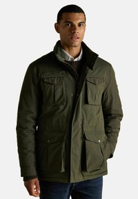 Zielona oliwka ocieplana kurtka z wysokim kołnierzem, z zamkiem błyskawicznym z przodu i czterema kieszeniami użytkowymi. Posiada gładką teksturę i akcenty z guzikami.