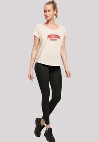 Light beige t-shirt with red "MORRIS MOTORS" graphic, paired with black leggings and black sneakers. Short sleeves, relaxed fit.