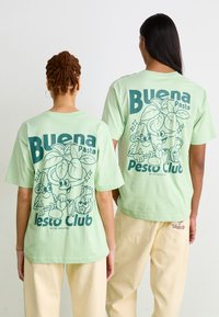 Majice kratkih rukava u mint zelenoj boji s razigranim grafičkim prikazom likova od hrane i natpisom "Buena Pasta Pesto Club" u tamnozelenoj boji.