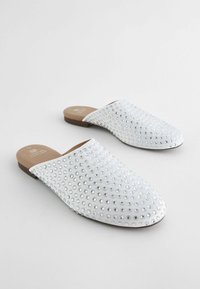 Vita slip-on mules med en slät yta, prydda med silver nitar som är jämnt fördelade, platt brun sula och rund tådesign.
