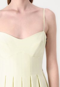 Rochie fără mâneci, de un galben deschis, cu decolteu în formă de inimă, design plisat și bretele subțiri. Țesătură netedă cu o textură subtilă și cusături.