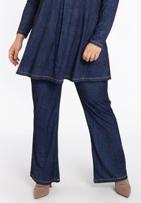 Dunkelblaue Denim-Tunika mit einem ausgestellten Saum und langen Ärmeln, kombiniert mit passenden dunkelblauen Denim-Hosen. Abgerundet mit kontrastierenden gelben Nähten.