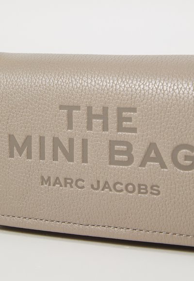 Taupe tekstureeritud nahk pinnal on sisse trükitud suurte tähtedega "THE MINI BAG MARC JACOBS".