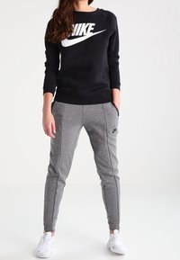 Black sweatshirt with white Nike logo, paired with gray tapered sweatpants featuring side seams and black logo, worn with white sneakers.