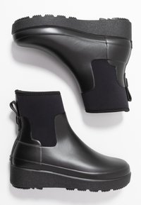 Une paire de bottes de chelsea noires imperméables avec des semelles en caoutchouc texturé et des panneaux élastiques sur les côtés, conçues pour les temps humides et un enfilage facile.