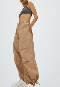 Beige, losse cargo-broek met elastische tailleband en trekkoord, voorzien van zijzakken en taps toelopende boorden. Gekocht met witte sneakers.