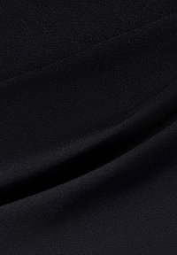 Svart tyg med en jämn, matt yta som har subtila vågor och veck. Inga tydliga mönster eller hårdvara syns.