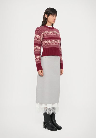 Pleteni bordo cropped pulover z napisom "HOLZWELL", kombiniran s sivo dolgo krilo z čipkasto obrobo. Črni škornji do kolen.