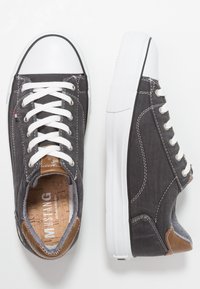 Šedé plátěné tenisky s bílými gumovými špičkami a šněrováním, které mají hnědé kožené detaily a texturovanou podrážku.