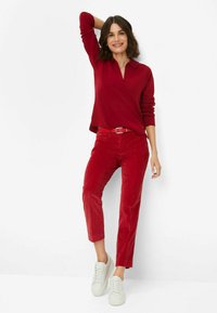 Roter Pullover mit Kragen, kombiniert mit passenden roten Cordhosen und weißen Sneakers; lässiger Schnitt mit glattem Material.