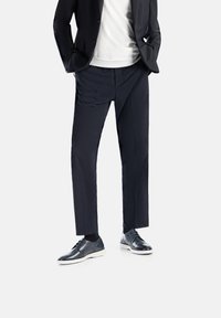 Pantaloni da cerimonia blu navy, vestibilità su misura, design a gamba dritta, abbinati a scarpe di pelle nera e una camicia bianca sotto un blazer scuro.