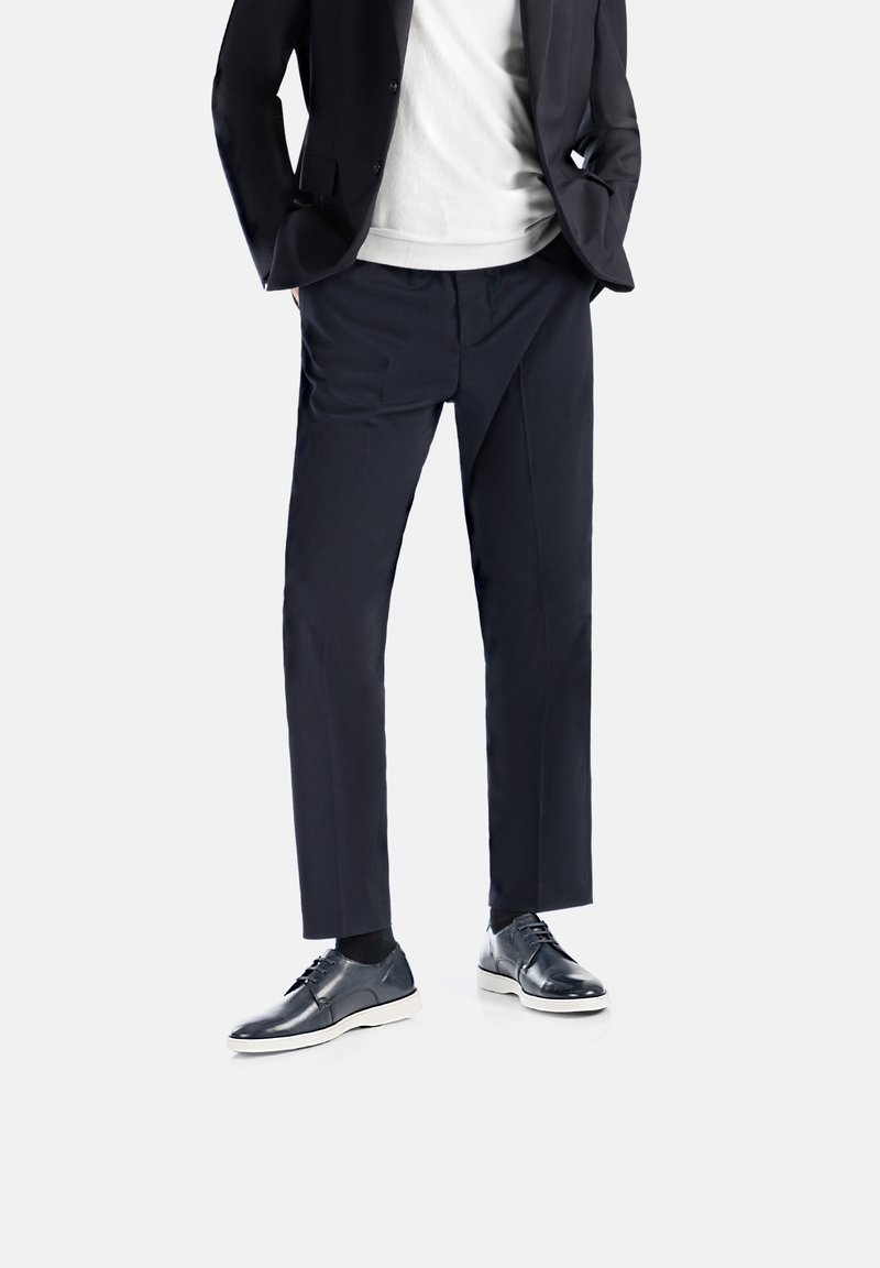 Pantaloni da cerimonia blu navy, vestibilità su misura, design a gamba dritta, abbinati a scarpe di pelle nera e una camicia bianca sotto un blazer scuro.