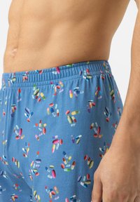 Blauwe shorts met een kleurrijk pillenpatroon, voorzien van een elastische tailleband en een zachte textuur. Het ontwerp bevat verschillende vormen en maten van pillen.