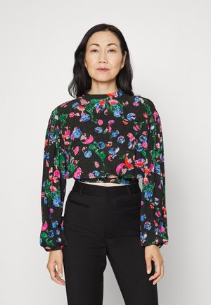 Blusa preta curta com mangas longas, apresentando um padrão floral em cores vibrantes. Combinada com calças pretas ajustadas.