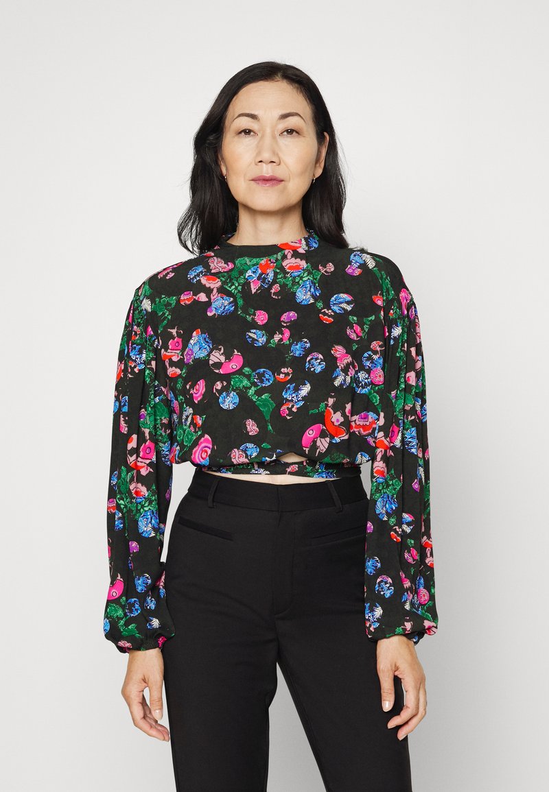 Blusa preta curta com mangas longas, apresentando um padrão floral em cores vibrantes. Combinada com calças pretas ajustadas.