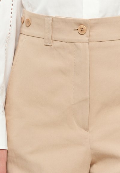 Beežid püksid, mis on tehtud puuvillast twill-kangast, siledat tekstuuri, kaks esimest taskut ja kaks pruuni nuppu vööl.