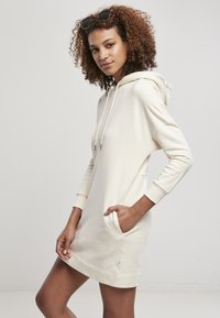 Rochie cu glugă din crem, fabricată dintr-un material moale, având mâneci lungi, buzunar tip kenguru și manșete ribbate. Design simplu și versatil.