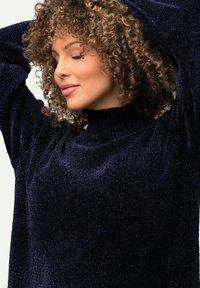 Pull en marine foncé avec un tissu texturé et moelleux ; col haut ; manches amples ; présentant une apparence douce et confortable.