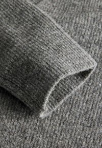 Tejido de suéter de punto gris con un acabado texturizado, mostrando una manga doblada y una apariencia suave y peluda.
