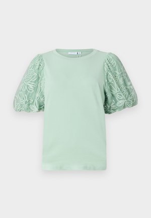 T-shirt verde menta con maniche corte e bombate, caratterizzato da un ricco ricamo bianco. Collo rotondo e texture morbida. Design semplice e contemporaneo.