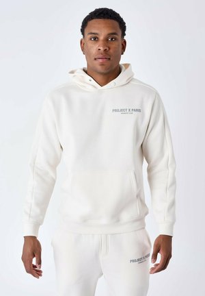 Sudadera de color beige claro hecha de una tela suave con un bolsillo tipo canguro, que presenta el texto gris "PROJECT X PARIS MEMBERS' CLUB" en la parte frontal.