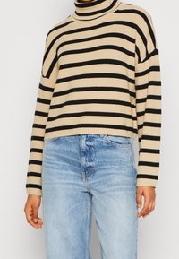 Pull à col roulé beige et noir à rayures, avec une texture côtelée, design court, associé à un jean taille haute bleu clair.