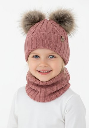 Bambino sorridente che indossa un cappello di lana rosa con due pon pon di pelliccia e una sciarpa abbinata, vestito con una maglia bianca a maniche lunghe.