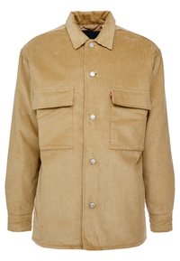 Tan kordflöjtsjacka med knäppning framtill, två bröstfickor och ribbad textur. Silverknappar och krage fulländar designen.