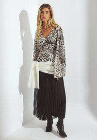 Long-sleeve wrap top with a grey and black animal print, paired with a pleated black skirt, and knee-high black heeled boots. White sash accent.