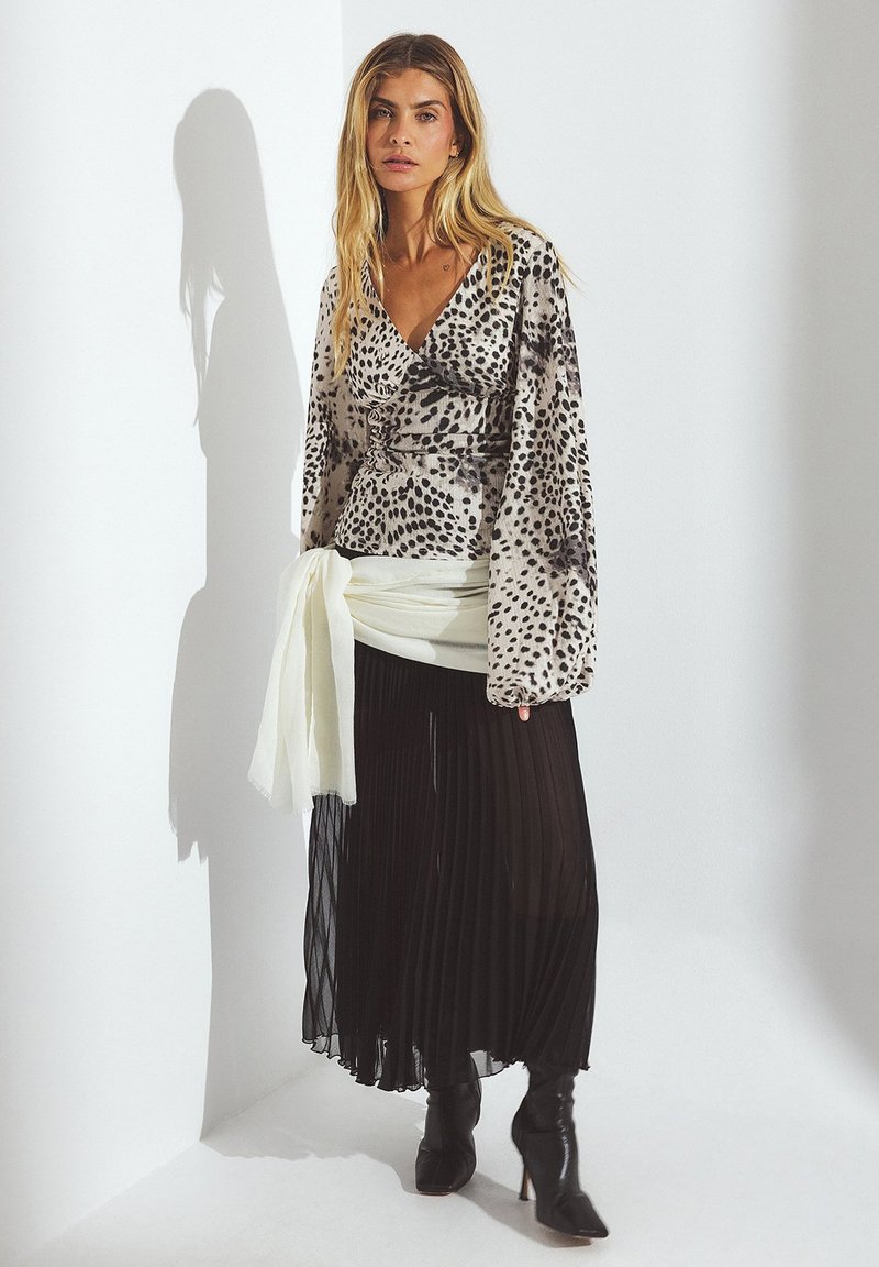 Long-sleeve wrap top with a grey and black animal print, paired with a pleated black skirt, and knee-high black heeled boots. White sash accent.