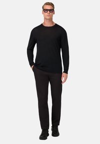 Črna majica z dolgimi rokavi iz lahkega materiala, v kombinaciji z temnimi hlačami in črnimi supergami. Model nosi prevelike črne sončne očala.