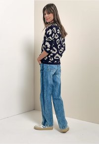 Marineblauer Pullover mit cremefarbenem Leopardenmuster, kombiniert mit hellblauen weit geschnittenen Jeans und beigen Sneakers mit hellblauen Akzenten.