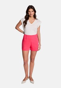 Witte V-hals top met versieringen, gecombineerd met hoog-waisted roze shorts met voorzakken en knoopaccenten.