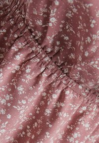 Tessuto a fantasia floreale in rosa polveroso, con piccoli fiori bianchi e una texture arricciata lungo l'elastico in vita.