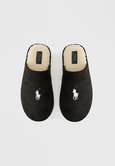 Mocasines de ante negro sin cordones con forro de lana de color crema y un logo bordado de jugador de polo blanco en la parte superior de cada zapatilla.