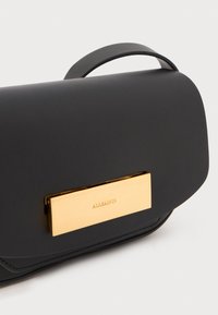 Borsa a tracolla nera in pelle con un fermaglio in metallo dorato rettangolare inciso con "ALLSAINTS" e una maniglia corta. Texture liscia.