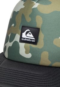 Tarnkappenmütze mit einem grün-beigen Muster, schwarzem Schirm mit gerippter Textur und einem rechteckigen schwarzen Quiksilver-Logo-Patch.