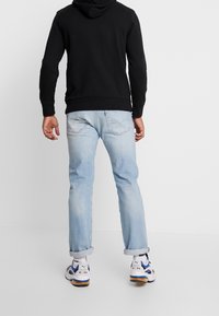 Sweat-shirt à capuche noir, jean bleu clair avec ourlets retroussés, et baskets blanches avec des accents bleus. La tenue présente un design minimaliste.