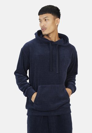 Hoodie en velours côtelé bleu marine avec une grande poche avant, capuche à cordon de serrage et texture côtelée. Comprend des manches longues et une coupe décontractée.