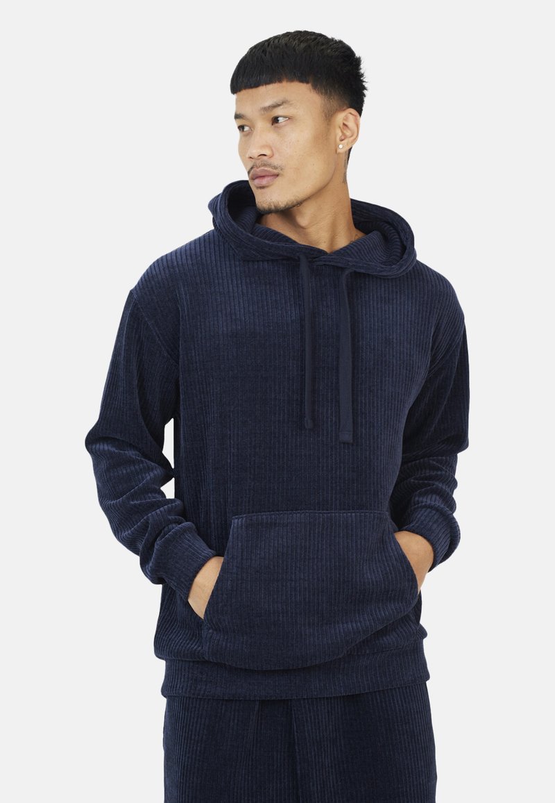 Marineblauwe corduroy hoodie met een ruime voorzak, trekkoordkap en geribbeld textuur. Heeft lange mouwen en een ontspannen pasvorm.