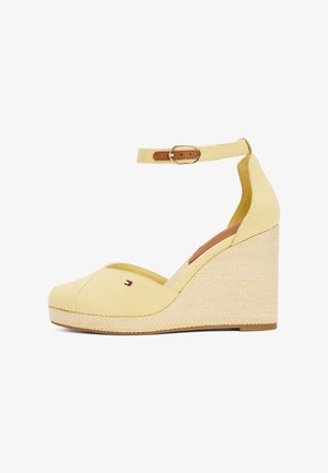 Sandalias de cuña de lienzo amarillas que presentan una puntera redondeada, una correa de tobillo con hebilla y una plataforma de estilo espadrille texturizada. Detalle del logo pequeño presente.