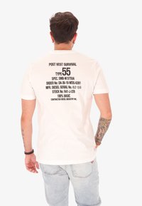 T-shirt bianco con testo nero, con dettagli del prodotto sul retro, colletto rotondo, maniche corte e vestibilità rilassata.