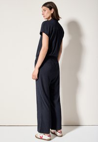 Navyblauwe tweedelige outfit met een textuurrijke, korte mouw top en wijde broekspijpen. Gecombineerd met lage sneakers in cr�ème, rood en bruin.