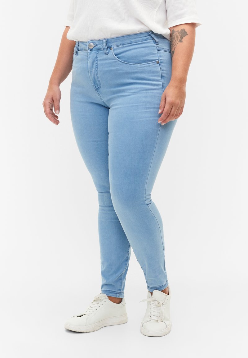 Vaqueros ajustados de color azul claro hechos de denim, con un diseño clásico de cinco bolsillos y cierre frontal de botón, combinados con zapatillas blancas.