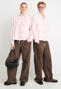 Ροζ ριγέ σακάκια με κορδέλες, συνδυασμένα με καφέ παντελόνια φαρδιάς γραμμής. Μαύρη τσάντα ώμου και χοντρά μαύρα παπούτσια ολοκληρώνουν την εμφάνιση.