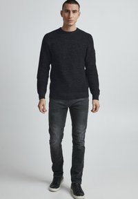 Maglione nero a maglia con un motivo testurizzato, colletto rotondo e maniche lunghe, abbinato a jeans slim-fit grigio scuro e sneakers nere.