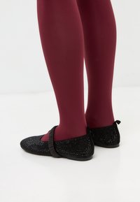 Zapatos planos negros con adornos de rhinestone texturizados, una correa flexible y una suela suave, combinados con medias burdeos.